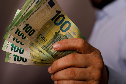 A hand holding multiple one hundred euro notes, symbolizing wealth and currency