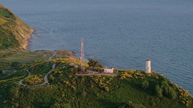 Aerial view of a lighthouse and communication tower on a green hill with yellow flowers in the Vjose-Narte Delta Protected Area, Zvernec, Vlore County, Albania.