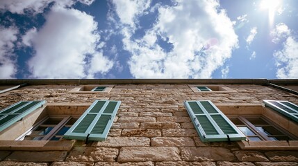 Obraz premium Traditional stone house facade revealing old masonry texture with open green shutters under a bright summer sky