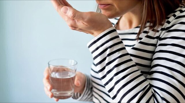 Woman taking medicine with a glass of water, following a daily regimen of treatment and healthcare at home