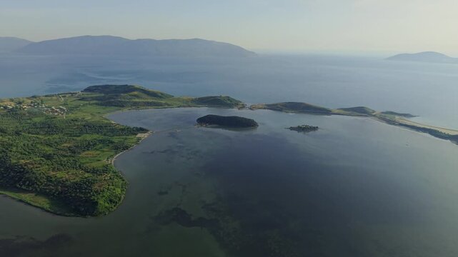Aerial view of the Vjose - Narte Delta Protected Area featuring the Narta Lagoon and Zvernec Island with lush green hills and calm waters in Zvernec, Vlore County, Albania.
