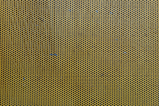 Close-up view of a yellow perforated metal surface, industrial texture background.