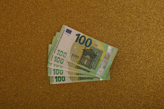 Group of hundred euro banknotes fanned out on a sparkling gold surface.