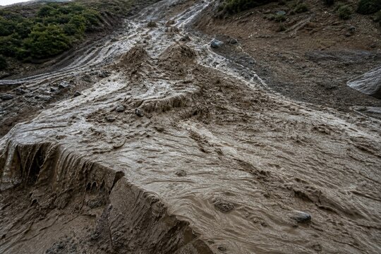 tonalite. Muddy slurry flowing down a hillside, creating viscous patterns in natural daylight. ESG reports, sustainability campaigns, designed for environmental awareness campaigns.