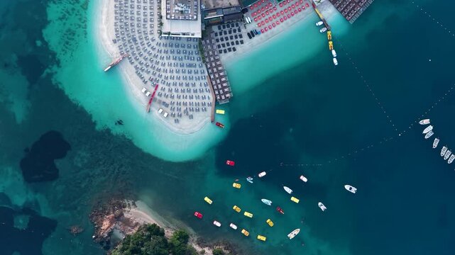 Aerial view of a white sand beach with sunbeds and umbrellas next to turquoise water and colorful boats in Ksamil, Vlore County, Albania.