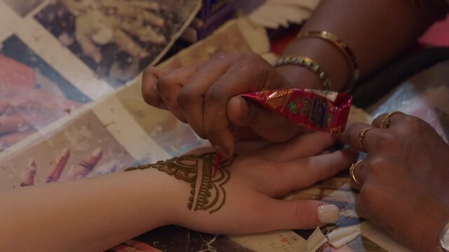 Closeup of artist applying a Mehandi tattoo on a woman's hand, beautiful, intricate with flowers. Indian traditional henna designs for celebration and cultural expression. 