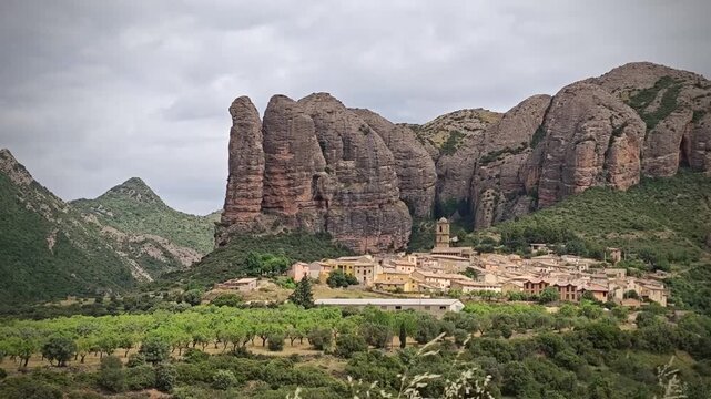 Aguero village in Spain is surrounded by the impressive rock formations known as "Mallos de Aguero." Nestled at the base of these towering, rugged cliffs, the village features traditional stone houses