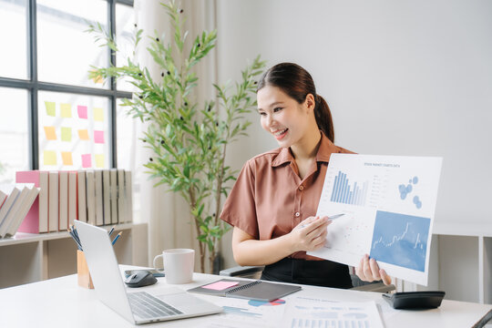 Businesswoman Presenting Financial Data: A focused businesswoman, sitting at her desk, confidently presents charts and graphs to an unseen audience via video call.