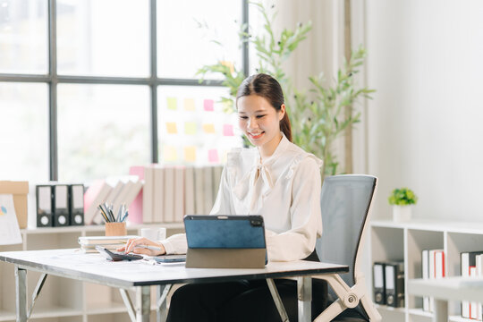 Focused Professional at Desk: A young woman, diligently working at her desk with a tablet and calculator, conveys concentration and productivity in a modern office setting.