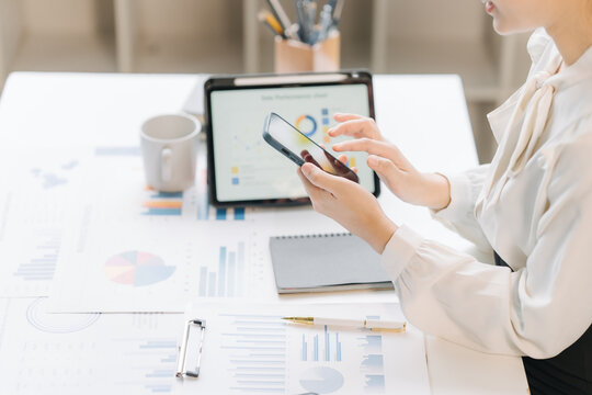 Analyzing Financial Data: A focused professional analyzes charts and graphs on a tablet and smartphone, surrounded by financial reports, representing data-driven decision-making in business.