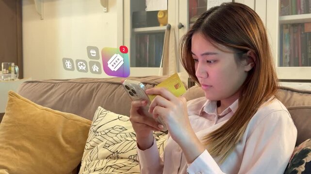 Southeast Asian woman buys event vouchers on phone with credit card on sofa, displaying 3D tracked ticket notification, gift box, and theme park badges.
