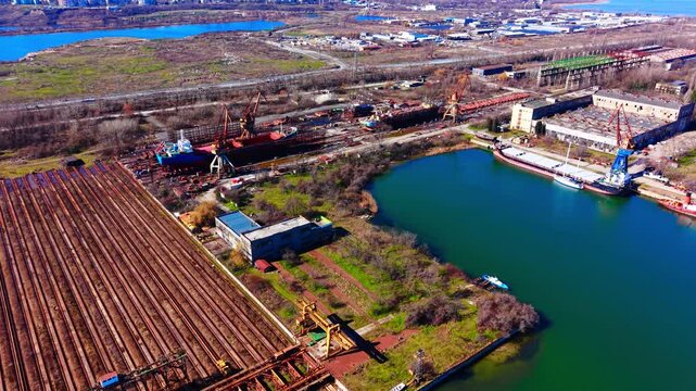 Scale view of a marine railway shipyard facility. Aerial overview of vessel repair tracks, heavy cranes, dry dock zone and calm sea water.