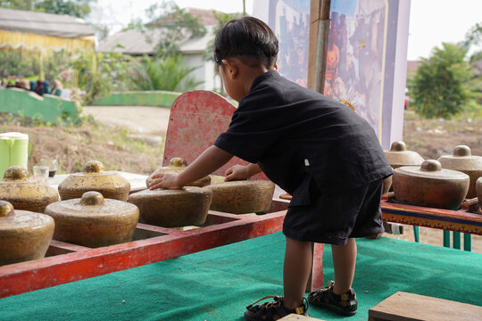 Excited young child playing a traditional Indonesian kenong instrument while learning traditional music, highlighting cultural heritage and early childhood education