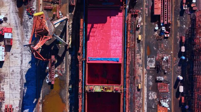 Overhead perspective of an empty bulk carrier hatch. Straight down aerial look into the deep red steel cargo hold and geometric deck structure.