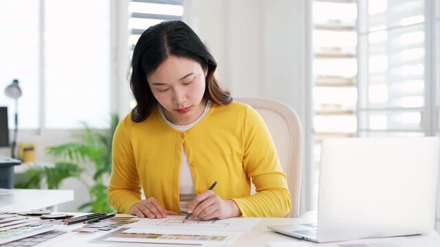 Creative female designer works on apartment design draws sketches in notebook surrounded by samples material and stationery