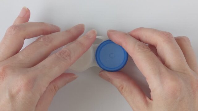 Contact lens container close up. Woman's hand unscrews the left lid of a contact lens container for a lens in her left eye. Concept for eye care and hygienic lens storage