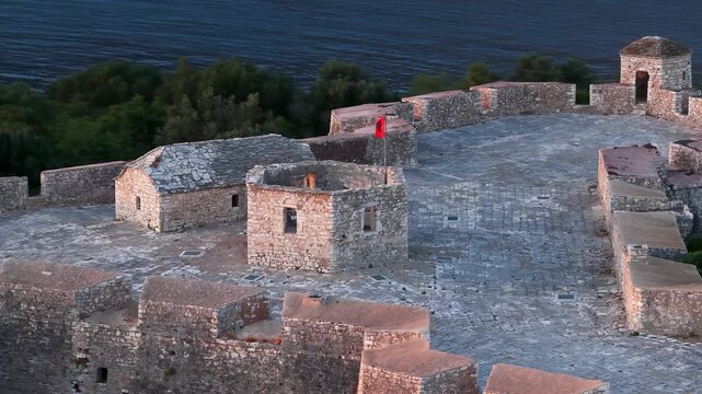 Aerial view of Porto Palermo Castle with its historic stone walls and a red flag waving above the Adriatic Sea in Porto Palermo, Qarku i Vlores, Albania.