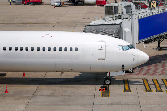 View front side nose passenger plane stands parking the terminal, waiting for to board via a jet bridge.