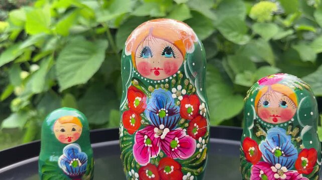 Matryoshka Dolls: A trio of colorful Matryoshka dolls, showcasing intricate floral patterns and cheerful faces, are displayed outdoors amidst lush green foliage.