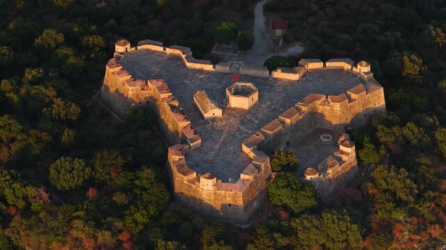 Aerial view of the triangular Porto Palermo Castle surrounded by dense green forest during golden hour in Porto Palermo, Qarku i Vlores, Albania.