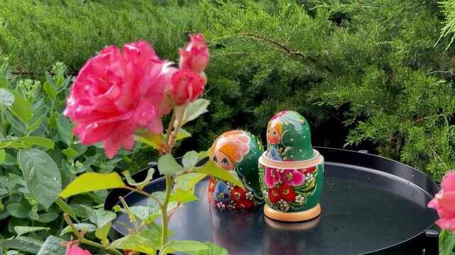 Russian Nesting Dolls in Bloom: Delicate Russian nesting dolls, adorned with vibrant floral patterns, are nestled among blooming pink roses and lush green foliage.