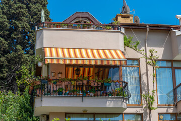 Balcony with plants and a striped awning in a residential area on a sunny day