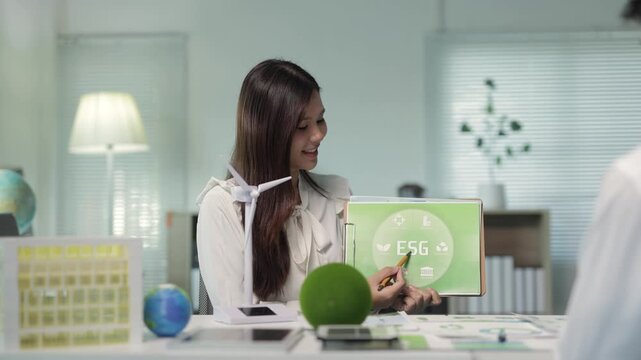 Professional businesswoman discussing a business plan for clean energy with colleagues, pointing to a document on a clipboard about environmental, social, and governance principles in a meeting