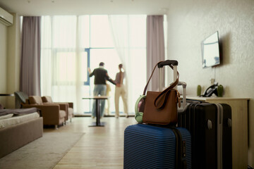 Obraz premium Wide angle view of young couple arriving in hotel room, unpacking luggage and starting vacation stay, checking view from window. Travel booking, hospitality marketing, family tourism promotion