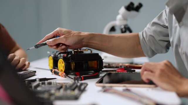 Young engineer's hands meticulously assembling a prototype robotic car using a screwdriver and various electronic components on a workbench in a technology laboratory or classroom setting
