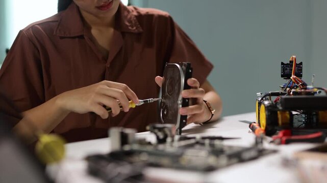 Young female technician using a screwdriver to disassemble and repair a computer hard drive while working on a robotics project in a science and technology laboratory for data recovery