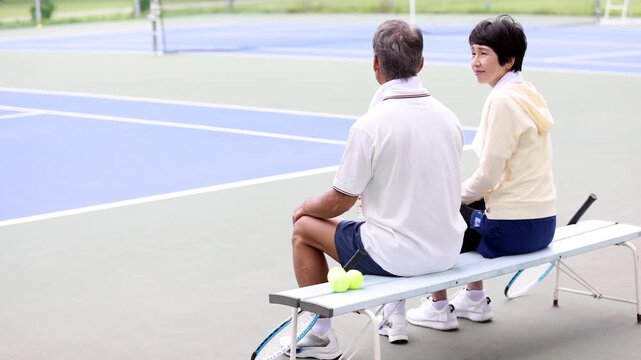 テニスコートのベンチで休憩するシニア夫婦の後ろ姿