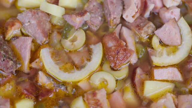 Homemade soup with sliced sausage and potato, golden broth with green pickle slices, closeup overhead simmering, cozy rustic atmosphere, hearty comfort food for chilly days