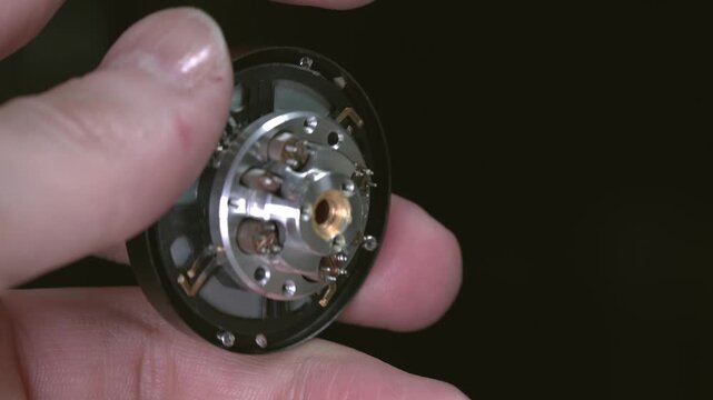 An engineer holds a disassembled VHS head drum with contacts for connecting to the board, viewed from the inside.