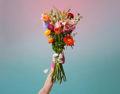 A bunch of flowers is being help aloft by and arm wearing a glove