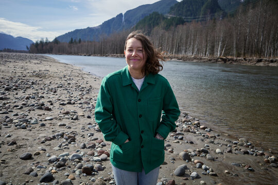 Woman stands by river with mountains in background during daylight
