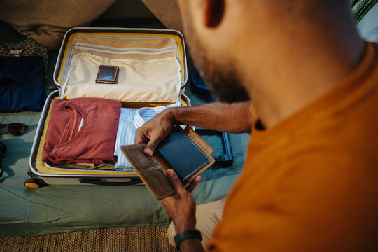 Man Checking Passport While Packing Suitcase for Travel