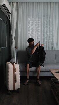Always working lifestyle and nonstop mobility. Man working on laptop on sofa with luggage, finishing work and leaving apartment immediately, vertical