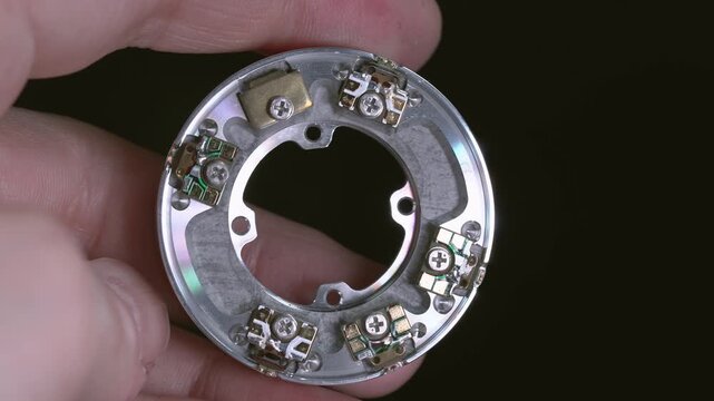 An engineer holds a disassembled VHS head drum with contacts for connecting to the board, viewed from the inside.