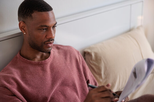 Man in bed reviews documents with pen.