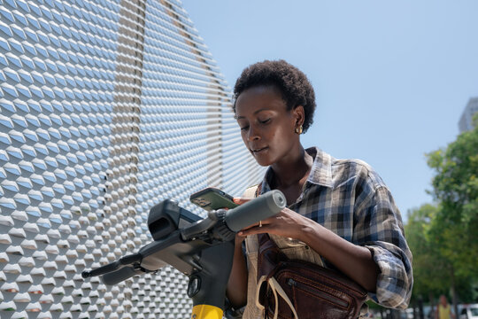 Young woman unlocking public e-scooter with her phone 