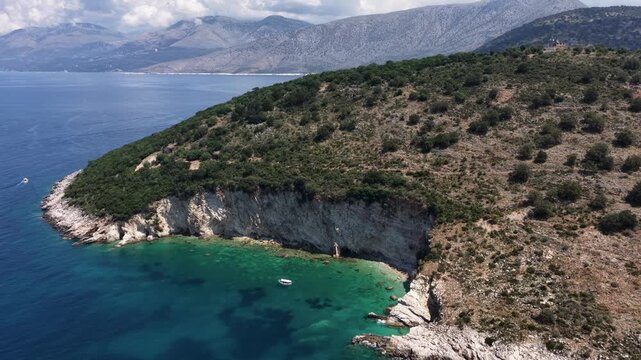 Aerial view of rocky cliffs and turquoise sea with a small boat near the coastline of Sarande, Vlore County, Albania.