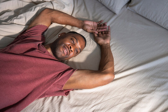 Man in bed, arms outstretched, looking at camera.