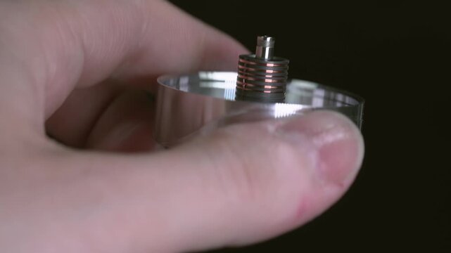 An engineer holds a disassembled VHS head drum with contacts for connecting to the board, viewed from the inside.