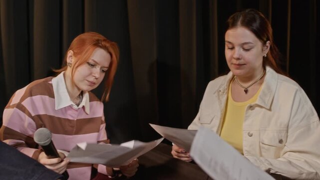 Panning shot of multiethnic teenagers rehearsing theater play script together on stage, holding papers and microphone. Clip for promoting high school drama clubs and creative arts education programs