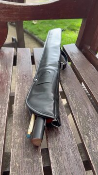 Vertical static close up view of professional pool cue stick in leather case on wooden bench