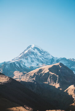 Snow peak Kazbegi rises above rugged terrain under blue sky