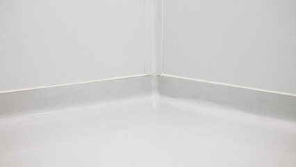Fototapeta premium Corner of a white room shows the seamless intersection where the wall meets the floor in a bright indoor setting.