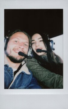 A couple wearing aviation headsets takes a selfie during a helicopter