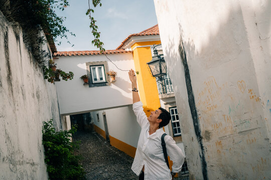 Visitor Walks in Narrow Street and Reaches for a Leaf in Portugal