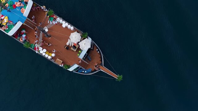 Aerial view of a tourist excursion boat with people on the wooden deck sailing on dark blue water in Sarande, Vlore County, Albania.